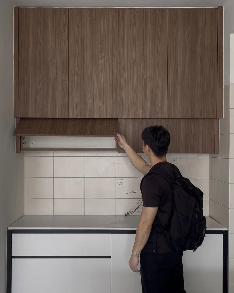Damon Cheong on site, testing the lift-up door of a newly installed wall cabinet above a kitchen counter.